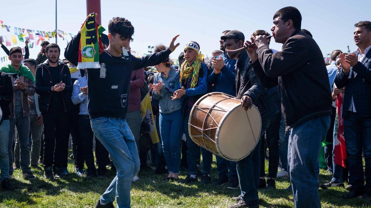 Ein junger Mann, in der rechten Hand mit einem Schal von Amedspor, die andere Hand zeigt das Siegeszeichen, tanzt vor mehreren anderen Männern in der südosttürkischen Stadt Diyarbakir zum kurdischen Neujahrsfest Newroz. Links neben ihm steht ein Mann mit einer großen Trommel. Ein junger Mann, in der rechten Hand mit einem Schal von Amedspor, die andere Hand zeigt das Siegeszeichen, tanzt vor mehreren anderen Männern in der südosttürkischen Stadt Diyarbakir zum kurdischen Neujahrsfest Newroz. Links neben ihm steht ein Mann mit einer großen Trommel.