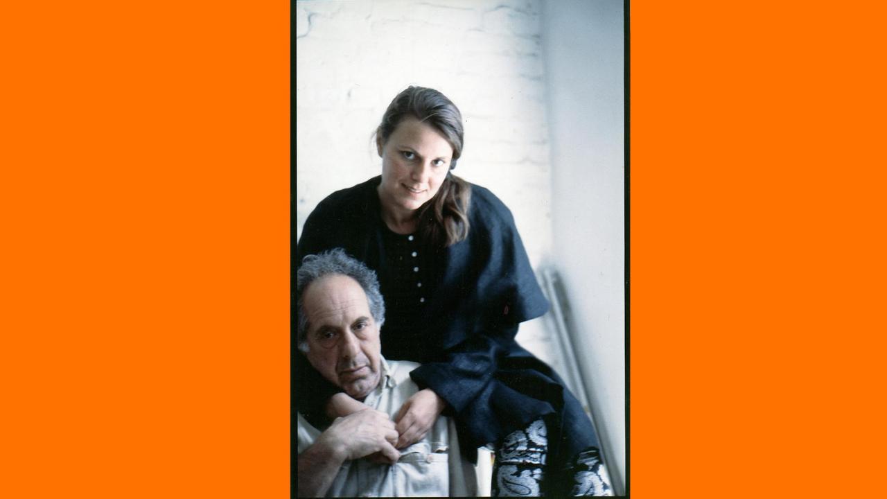 Gundula Schulze Eldowy sitzt auf der Lehne eines Stuhls und umarmt Robert Frank. Gundula Schulze Eldowy sitzt auf der Lehne eines Stuhls und umarmt Robert Frank.