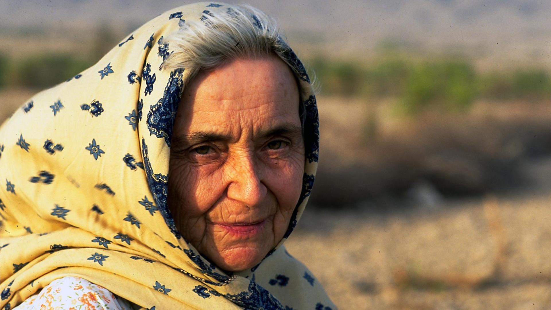 Ruth Pfau wird von der Sonne angestrahlt. Sie trägt ein gelb-blaues Tuch auf dem Kopf, das im Wind weht. Im Hintergrund ist Wüste. Ruth Pfau wird von der Sonne angestrahlt. Sie trägt ein gelb-blaues Tuch auf dem Kopf, das im Wind weht. Im Hintergrund ist Wüste.