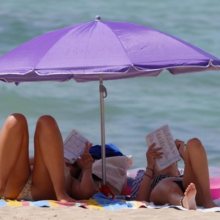 Zwei Frauen liegen am Strand "El Arenal" auf Mallorca unter einem Sonnenschirm