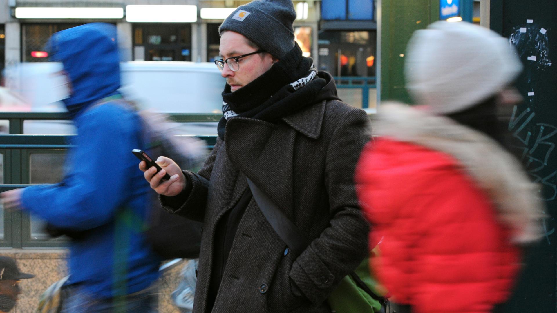 Ein junger Mann steht am 24.01.2015, mit dem Blick auf sein Smartphone gerichtet, an einer Straße in Berlin. Ein junger Mann steht am 24.01.2015, mit dem Blick auf sein Smartphone gerichtet, an einer Straße in Berlin.