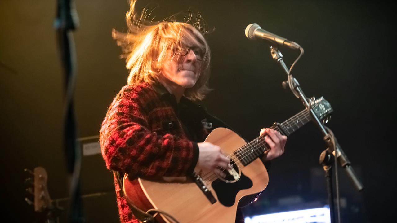 Ein Mann mit blonden wehenden Haaren hält eine Akustik-Gitarre in der Hand. Ein Mann mit blonden wehenden Haaren hält eine Akustik-Gitarre in der Hand.