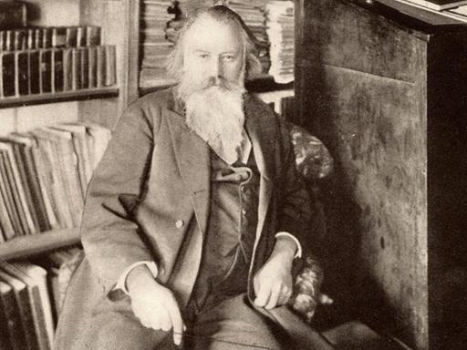 Der Komponist Johannes Brahms (1833-1897) sitzt auf einer zeitgenössischen Schwarz-weiss-Fotografie in seiner Bibliothek.