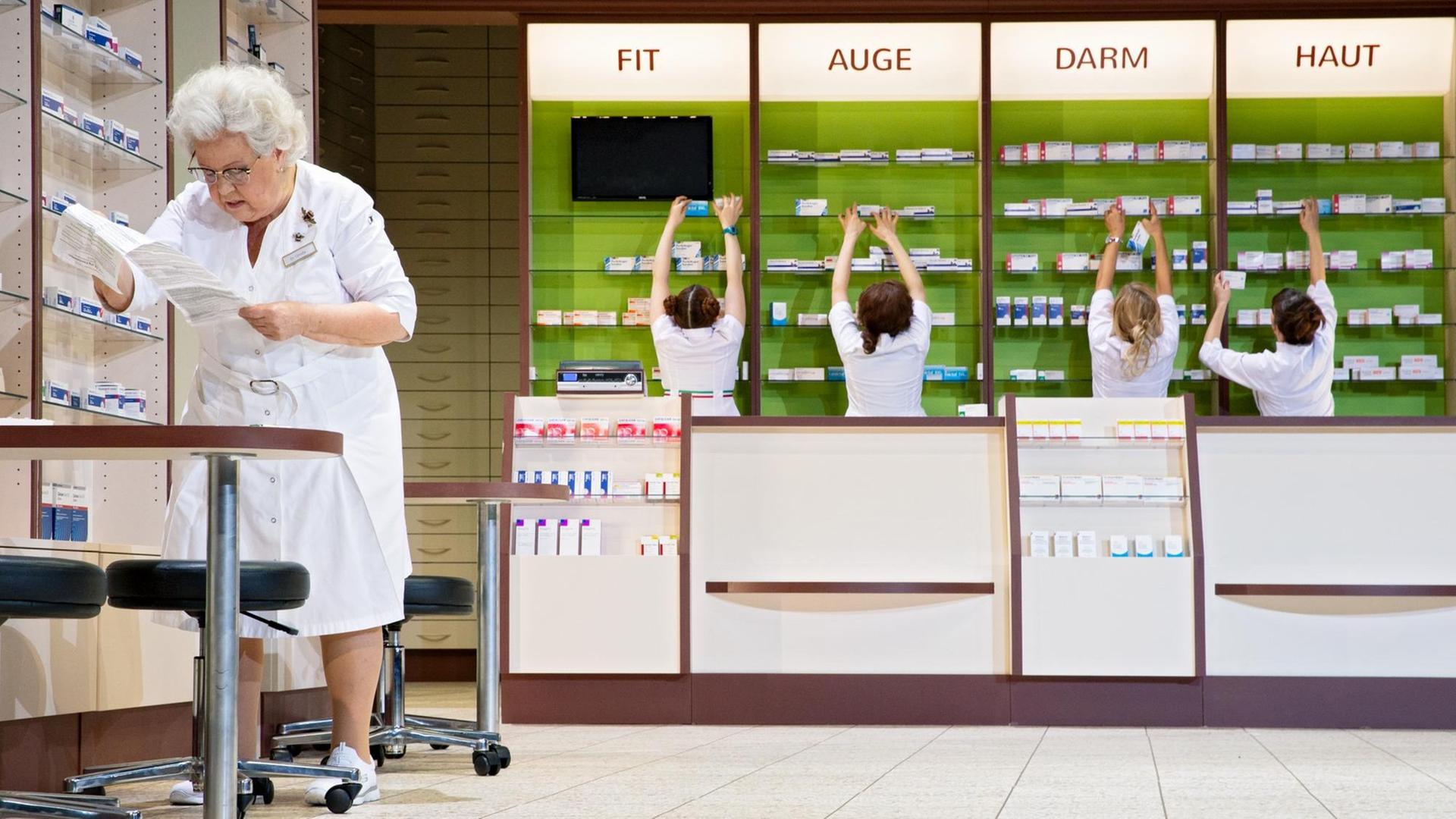 Szene aus Christoph Marthalers "Das Weinen" am Schauspielhaus Zürich: Auf der einer Apotheke ähnelnden Bühne sieht man links eine ältere Schauspielerin mit weißem Haar (Nikola Weisse), die Papiere studiert, während im Hintergrund an der Wand vier weitere jüngere Schauspielerinnen (Liliana Benini, Elisa Plüss, Susanne-Marie Wrage, Olivia Grigolli) an Medikamenten-Regalen herumräumen, über denen in Leuchtschrift von links nach rechts die Überschriften "FIT", "AUGE", "DARM" und "HAUT" stehen. Szene aus Christoph Marthalers "Das Weinen" am Schauspielhaus Zürich: Auf der einer Apotheke ähnelnden Bühne sieht man links eine ältere Schauspielerin mit weißem Haar (Nikola Weisse), die Papiere studiert, während im Hintergrund an der Wand vier weitere jüngere Schauspielerinnen (Liliana Benini, Elisa Plüss, Susanne-Marie Wrage, Olivia Grigolli) an Medikamenten-Regalen herumräumen, über denen in Leuchtschrift von links nach rechts die Überschriften "FIT", "AUGE", "DARM" und "HAUT" stehen.