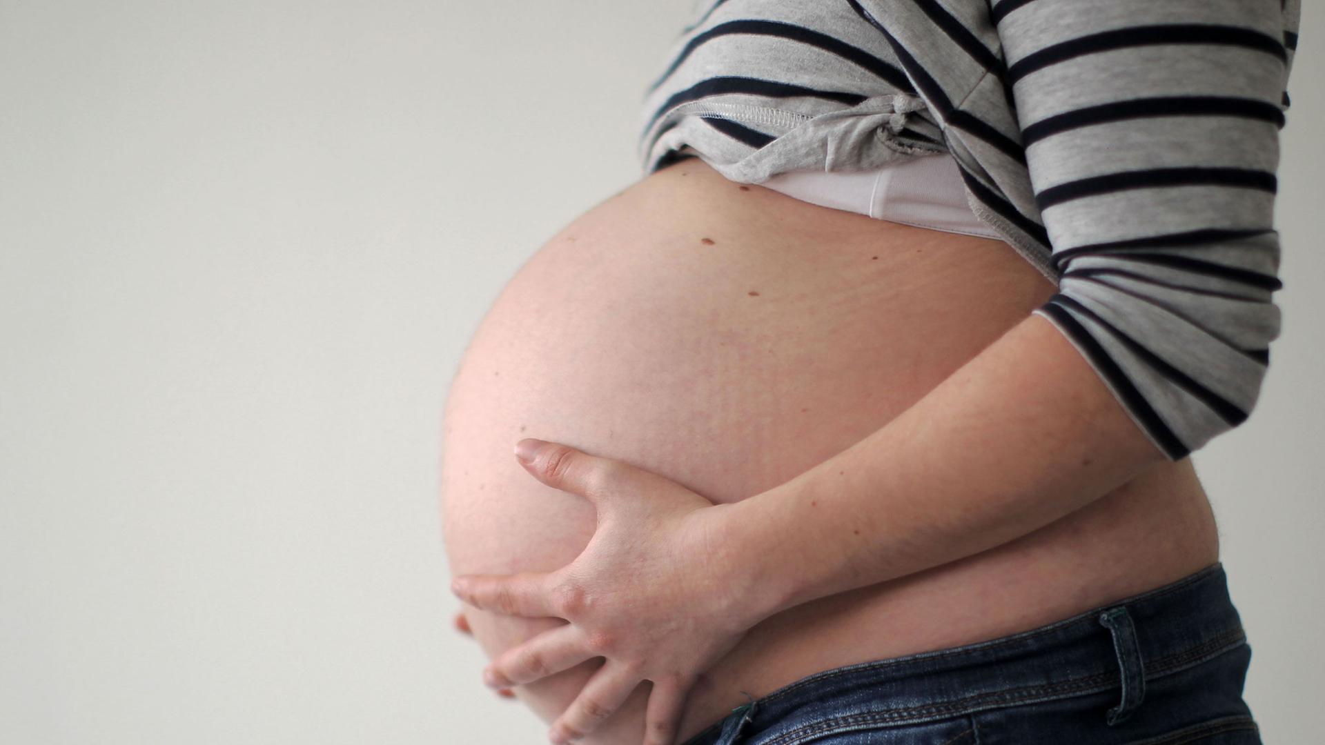 Eine schwangere Frau hält ihren Bauch. Eine schwangere Frau hält ihren Bauch.