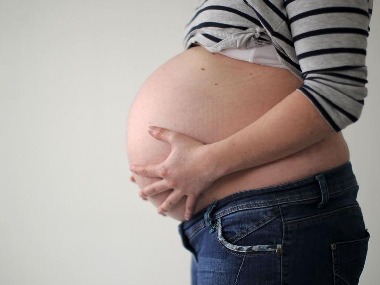 Eine schwangere Frau hält ihren Bauch.