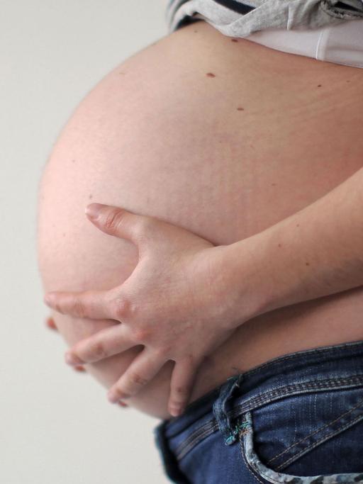 Eine schwangere Frau hält ihren Bauch.