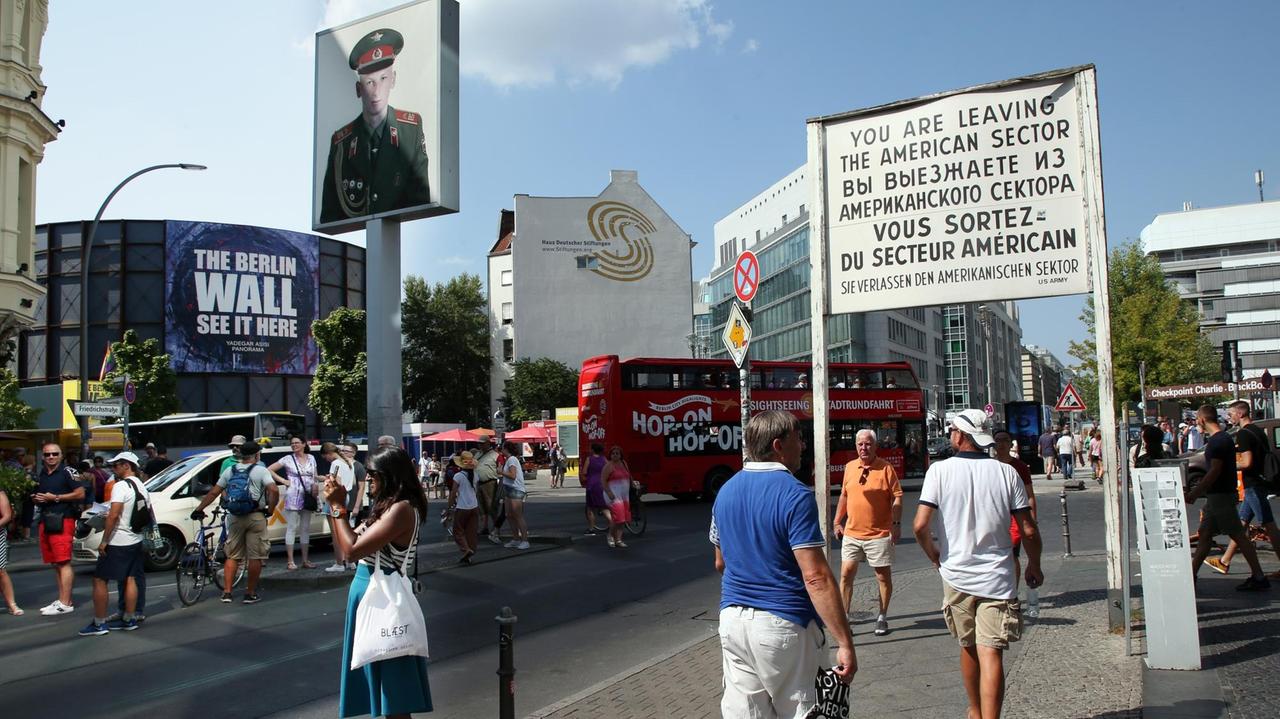 Touristen laufen am Checkpoint Charlie, dem ehemaligen Grenzübergang zwischen West- und Ostberlin, über die Straßen. Touristen laufen am Checkpoint Charlie, dem ehemaligen Grenzübergang zwischen West- und Ostberlin, über die Straßen.