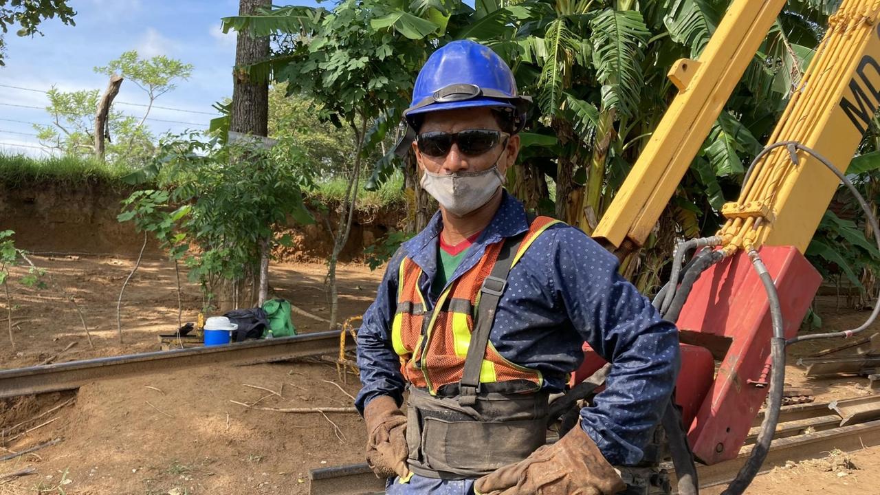 Ein Mann steht in Arbeitskleidung mit Sonnenbrille, Bauhelm und Mundschutz auf einer Baustelle. Ein Mann steht in Arbeitskleidung mit Sonnenbrille, Bauhelm und Mundschutz auf einer Baustelle.