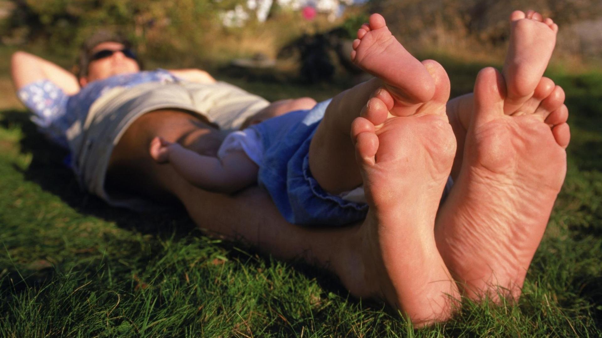Ein Vater und Kind liegen im Gras und ruhen sich, die Füße weit von sich gestreckt, aus. Ein Vater und Kind liegen im Gras und ruhen sich, die Füße weit von sich gestreckt, aus.