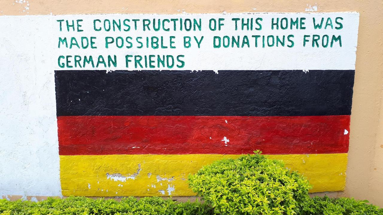 An eine Wand ist eine Deutschlandfahne gemalt, darüber die Aufschrift "The construction of this home was made possible by donations from German friends".