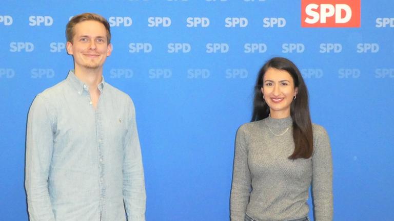 Zwei junge Menschen stehen vor einer Plakatwand. Zwei junge Menschen stehen vor einer Plakatwand.