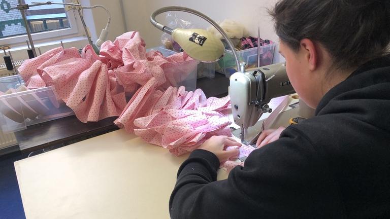 Eine Frau an einer Nähmaschine, die pinke Mundschutzmasken näht. Eine Frau an einer Nähmaschine, die pinke Mundschutzmasken näht.