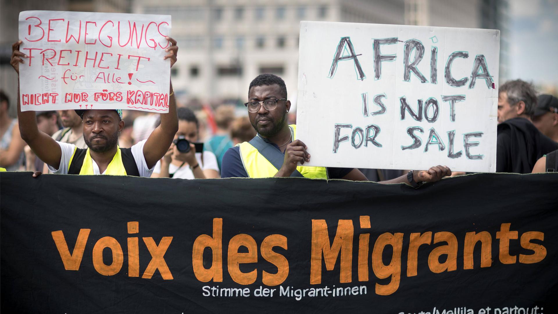 Vor Beginn der G20-Afrika Konferenz am 12.6.2017 wurde dagegen demonstriert. Die Menschen halten ein Schild mit der Aufschrift "Africa is not for sale" hoch. Ein anderes Schild zeigt die Aufschrift "Bewegungsfreiheit für alle – nicht nur fürs Kapital". Auf einem schwarzen Plakat ist außerdem zu lesen "Stimme der Migrant-innen" . Vor Beginn der G20-Afrika Konferenz am 12.6.2017 wurde dagegen demonstriert. Die Menschen halten ein Schild mit der Aufschrift "Africa is not for sale" hoch. Ein anderes Schild zeigt die Aufschrift "Bewegungsfreiheit für alle – nicht nur fürs Kapital". Auf einem schwarzen Plakat ist außerdem zu lesen "Stimme der Migrant-innen" .