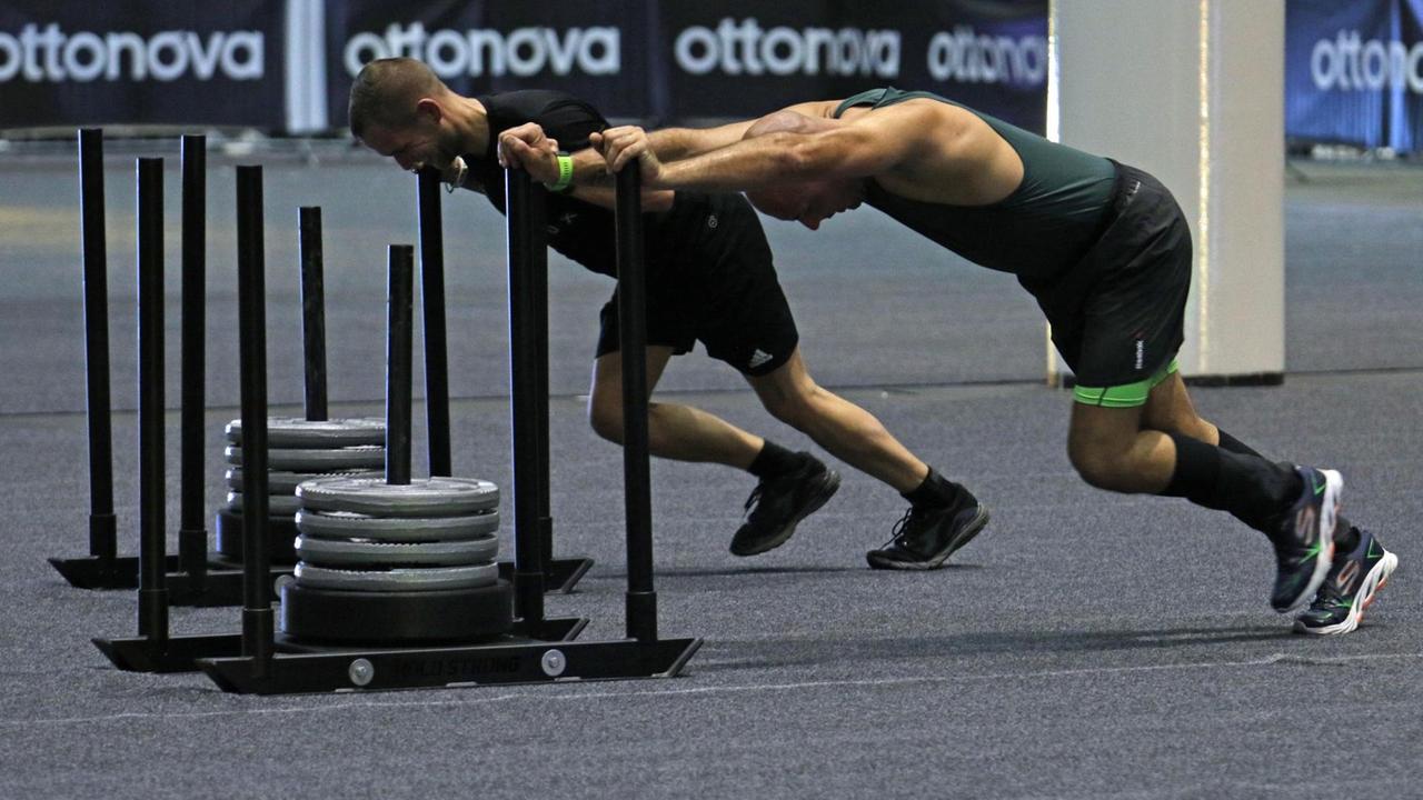 Zwei Sportler schieben beim Fitnesswettbewerb Hyrox in den Hamburger Messehallen Schlitten mit Gewichten. Zwei Sportler schieben beim Fitnesswettbewerb Hyrox in den Hamburger Messehallen Schlitten mit Gewichten.