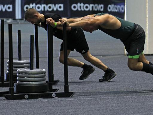 Zwei Sportler schieben beim Fitnesswettbewerb Hyrox in den Hamburger Messehallen Schlitten mit Gewichten.