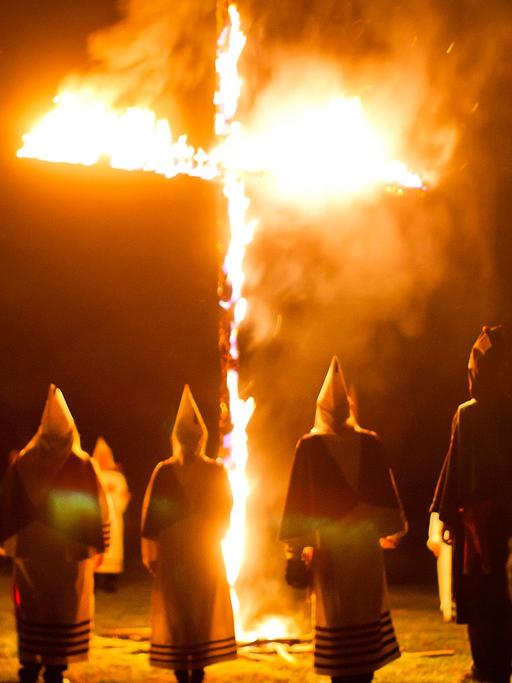 Mitglieder des Geheimbundes Ku-Klux-Klan in den USA stehen in weißen Gewändern und Kapuzen um ein brennendes Kreuz.