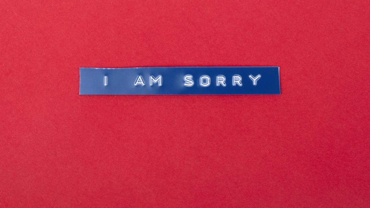 Auf rotem Untergrund liegt ein blauer Plastikstreifen auf den die Worte „I am sorry“ geprägt sind Auf rotem Untergrund liegt ein blauer Plastikstreifen auf den die Worte „I am sorry“ geprägt sind