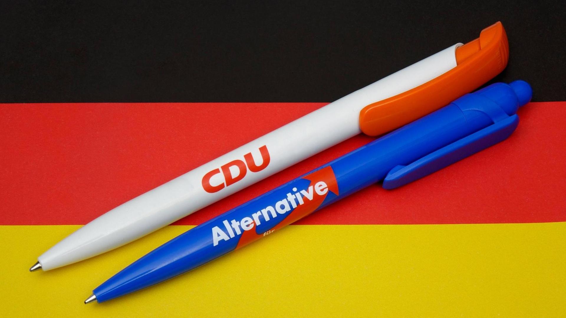 Kugelschreiber von CDU und AfD liegen auf einer Deutschlandfahne. Kugelschreiber von CDU und AfD liegen auf einer Deutschlandfahne.