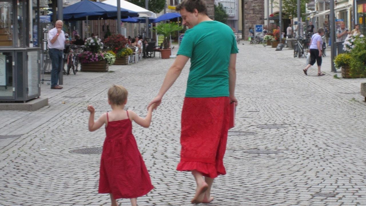 Nils Pickert läuft mit seinem Sohn die Straße entlang. Er trägt einen Rock, der Junge ein rotes Kleid. Nils Pickert läuft mit seinem Sohn die Straße entlang. Er trägt einen Rock, der Junge ein rotes Kleid.