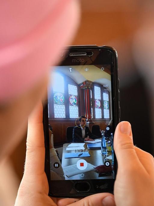 Eine Journalistin macht während einer Pressekonferenz mit ihrem Smartphone ein Foto.