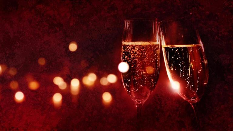 Zwei Champagnergläser vor einem festlichen roten Hintergrund, der in der Unschärfe liegt. Zwei Champagnergläser vor einem festlichen roten Hintergrund, der in der Unschärfe liegt.