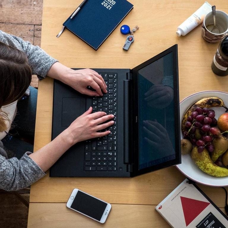Eine Frau sitzt zu Hause an einem Tisch und arbeiten an ihrem Laptop
