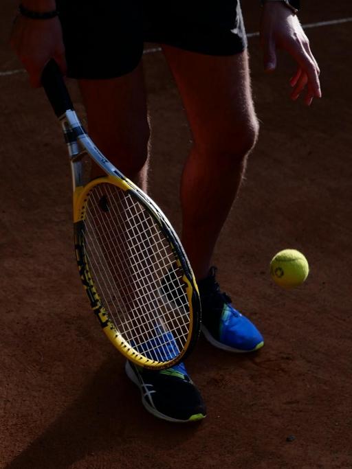 Ausschnitt eines Tennisspielers mit Schläger und Ball, der vom Sonnenlicht gestriffen wird.