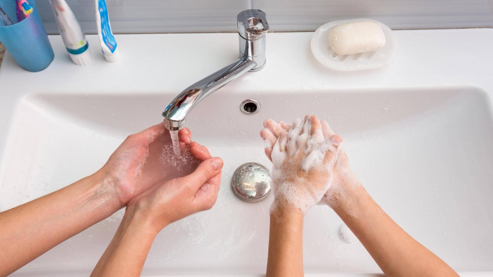 Ein Erwachsener und ein Kind waschen sich zuhause am Waschbecken die Hände. Ein Erwachsener und ein Kind waschen sich zuhause am Waschbecken die Hände.