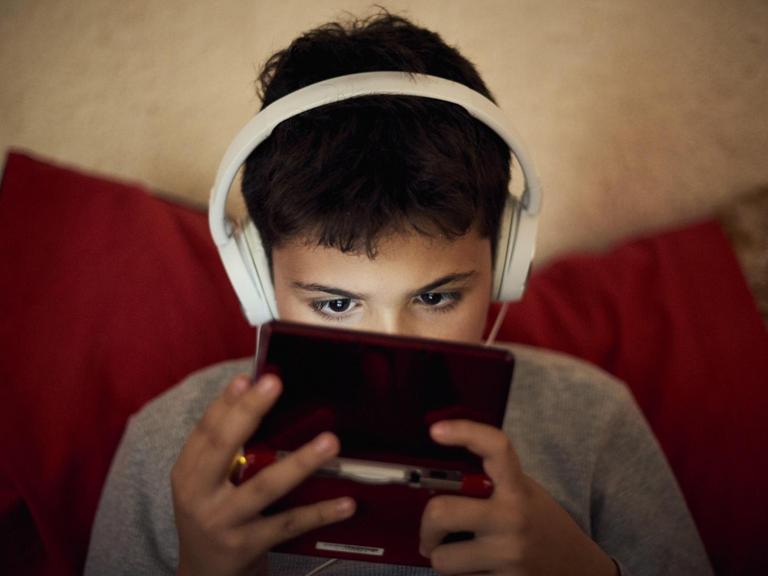Symbolbild: Kind schaut in Handy, Kopfhörer auf den Ohren