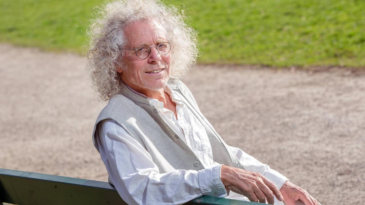 Rainer Langhans sitzt in München auf einer Parkbank und lächelt für eine Foto. Rainer Langhans sitzt in München auf einer Parkbank und lächelt für eine Foto.