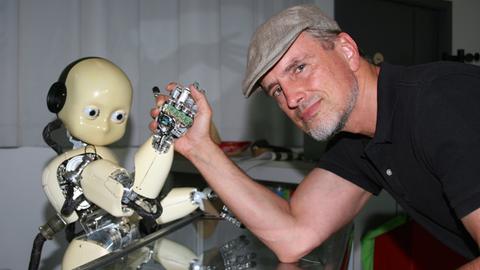 Der KI-Forscher Jürgen Schmidhuber beim Armdrücken mit einem Roboter