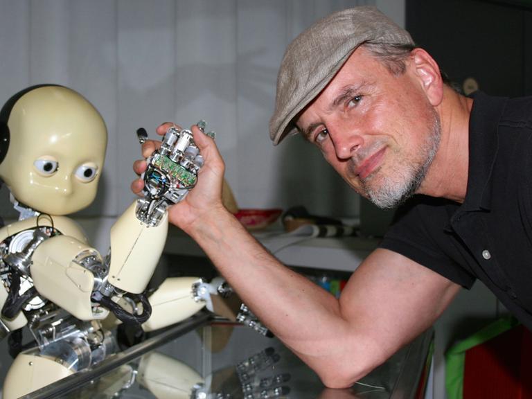 Der KI-Forscher Jürgen Schmidhuber beim Armdrücken mit einem Roboter