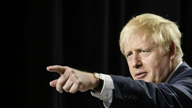 Der britische Premier Johnson zeigt mit seiner linken Hand in die Ferne.