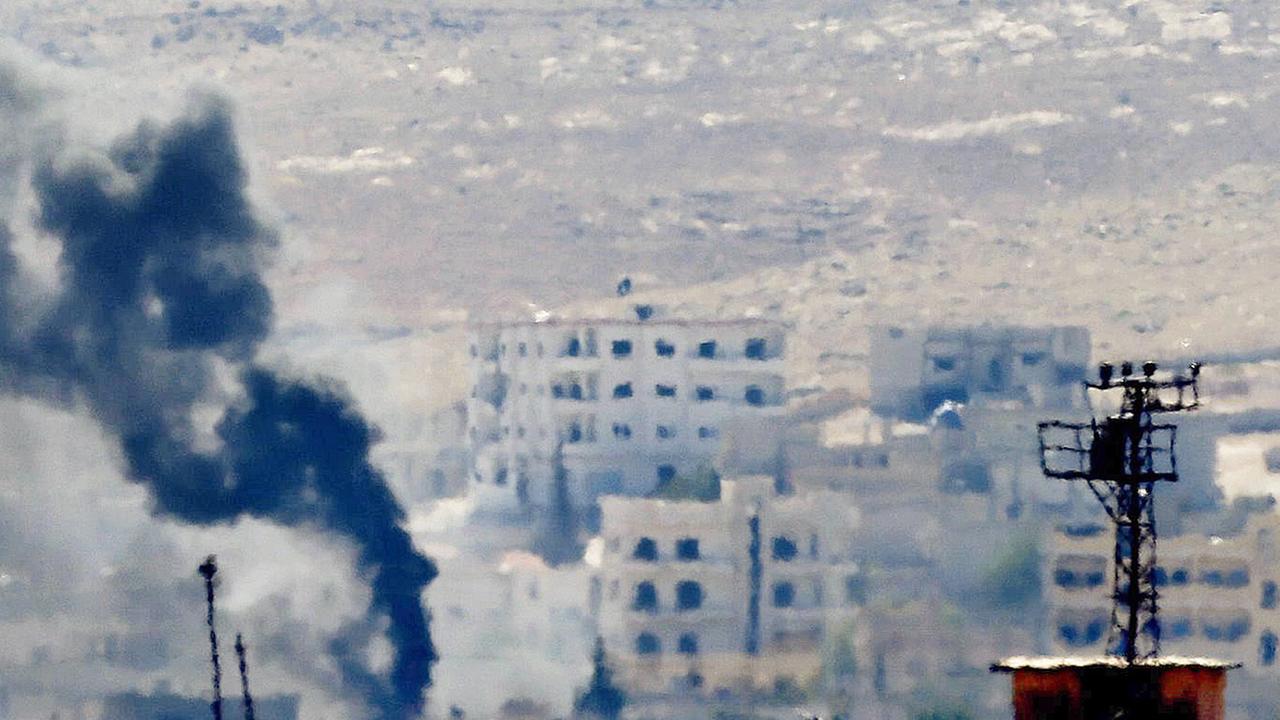 Leicht verschwommene Aufnahme mehrerer Gebäude in Kobane, aus denen Rauch aufsteigt. Leicht verschwommene Aufnahme mehrerer Gebäude in Kobane, aus denen Rauch aufsteigt.