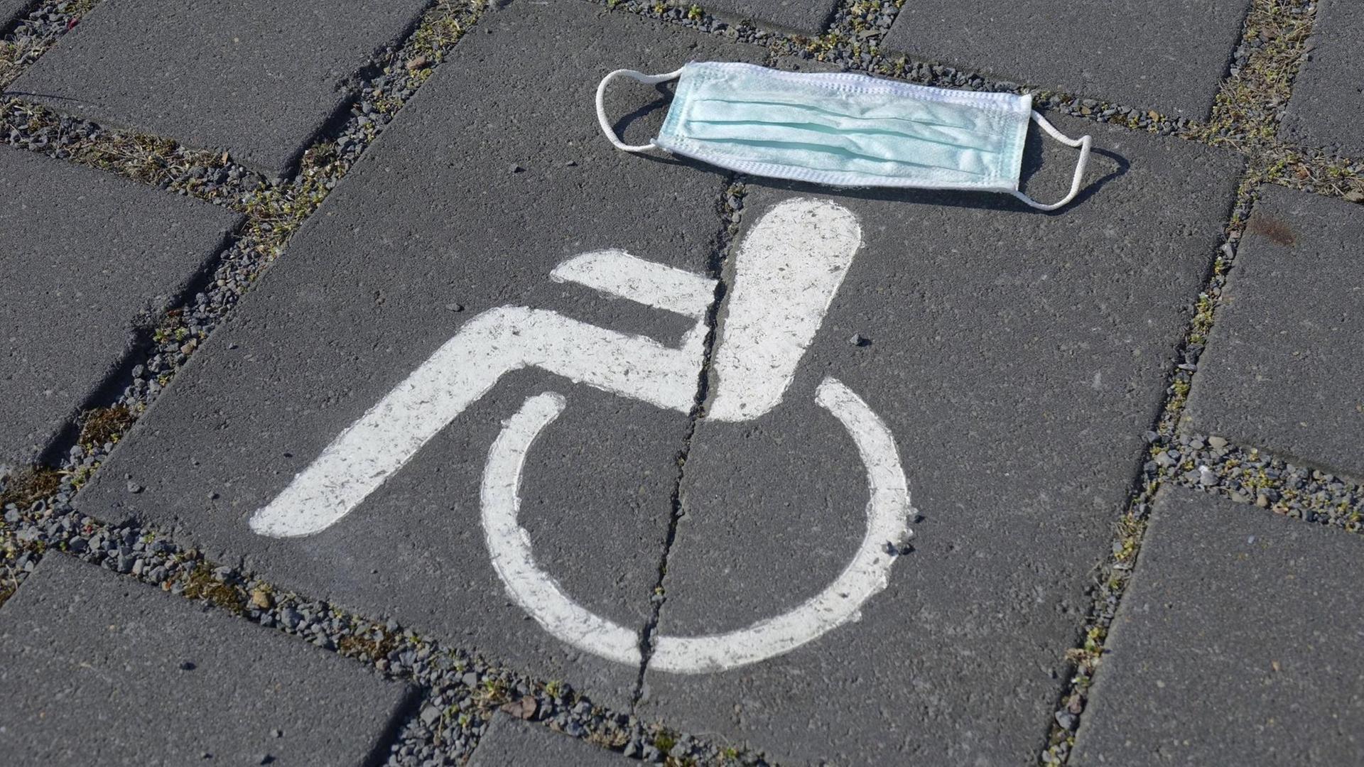 Symbol eines Behindertenparkplatzes, darüber ein Mundschutz Symbol eines Behindertenparkplatzes, darüber ein Mundschutz