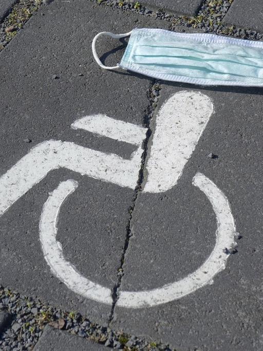 Symbol eines Behindertenparkplatzes, darüber ein Mundschutz