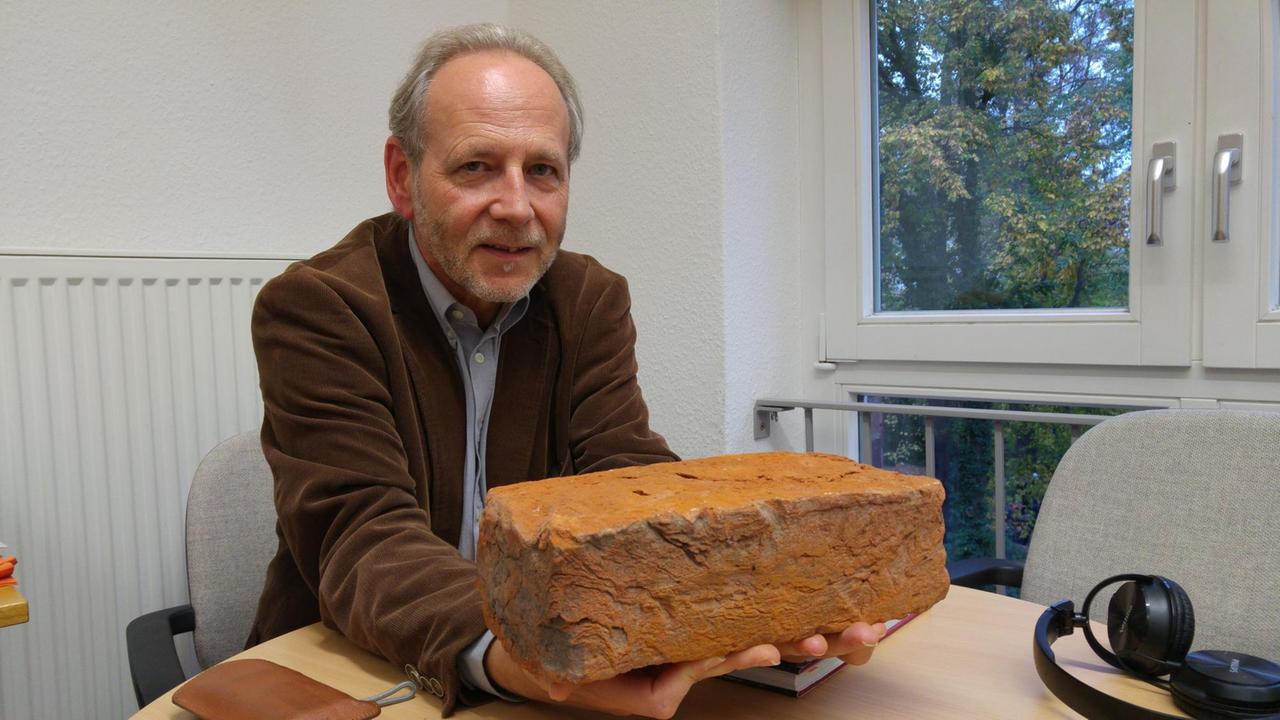 Der Greifswalder Kunsthistoriker Michael Lissok. Ein Mann sitzt an einem Tisch und hält einen Backstein in der Hand.