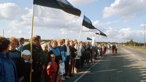 Menschen stehen mit Flaggen entlang einer Straße in Estland - ein Teil der mehr als 600 Kilometer langen Menschenkette durch die drei baltischen Republiken Lettland, Litauen und Estland im Jahr 1989.