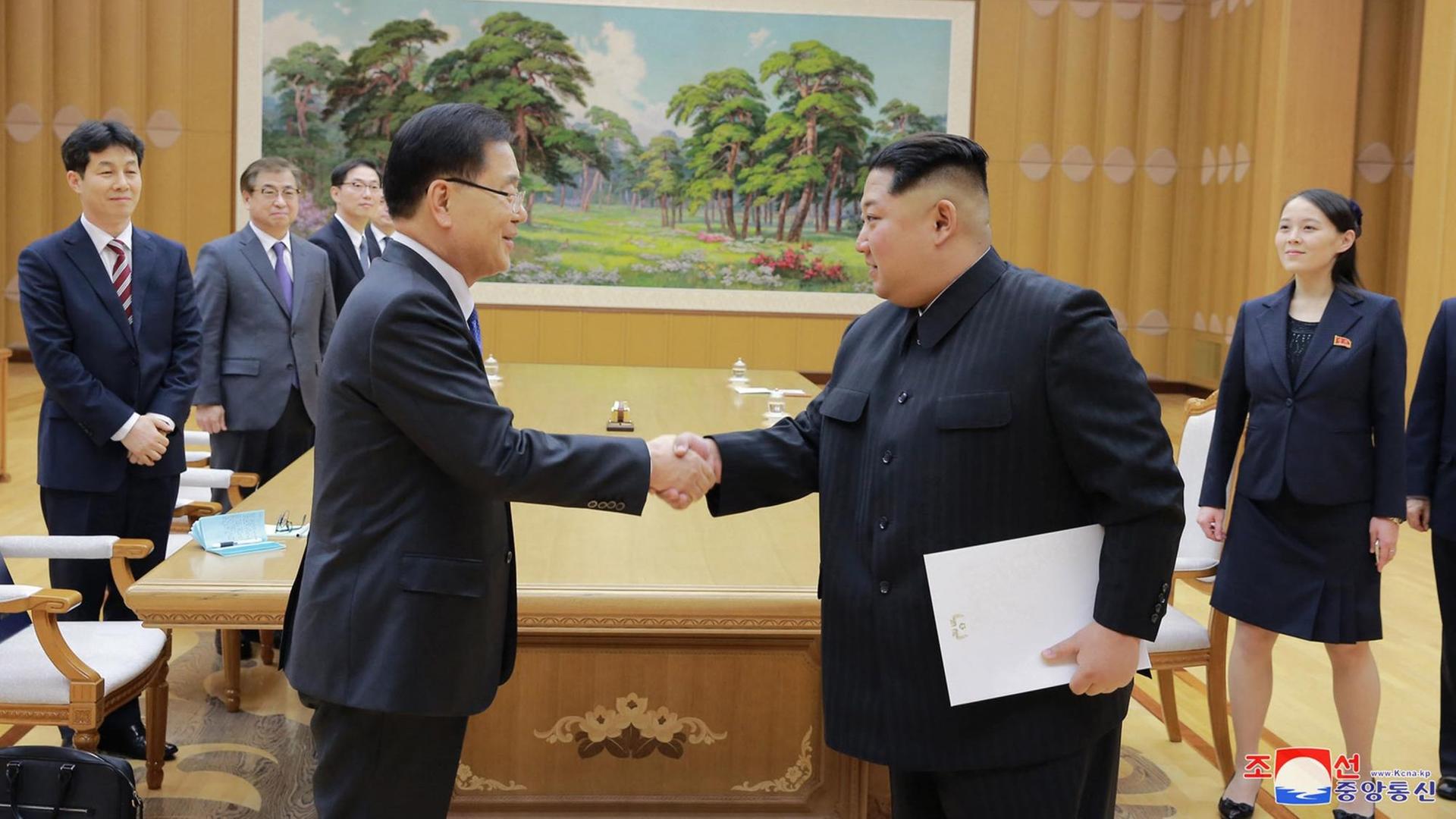 Der nordkoreanische Machthaber Kim Jong Un gibt einem Entsandten aus Südkorea die Hand. Im Hintergrund stehen weitere Personen. Der nordkoreanische Machthaber Kim Jong Un gibt einem Entsandten aus Südkorea die Hand. Im Hintergrund stehen weitere Personen.