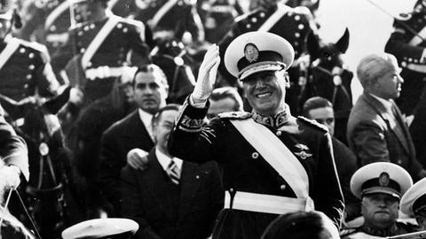 Der argentinische Präsident Juan Domingo Perón, uniformiert auf einer Militärparade, den Zusachuern mit der rechten Hand zuwinkend.