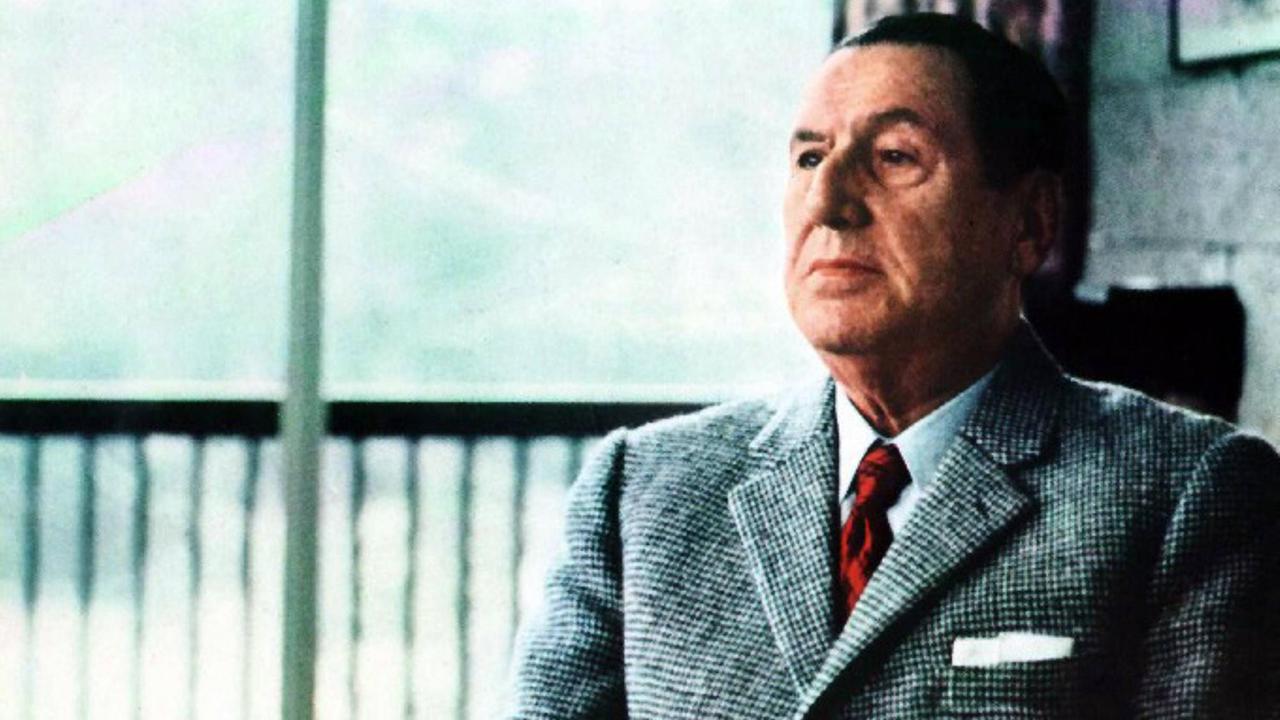 Historische Aufnahme von Juan Domingo Perón, der mit Anzug und Krawatte vor einem Fenster sitzt.