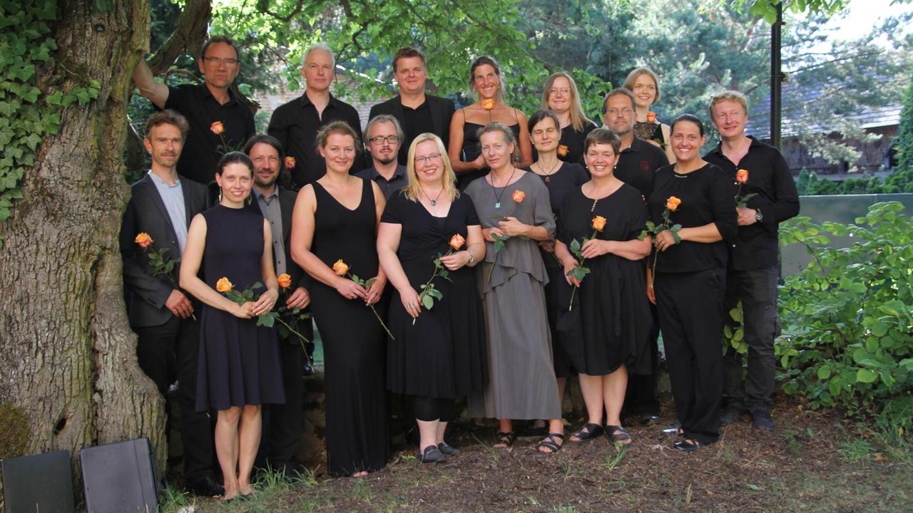 Ein Gruppenbild des Chores in schwarzer Chorkleidung. Der Chor steht unter zwei großen Bäumen. Ein Gruppenbild des Chores in schwarzer Chorkleidung. Der Chor steht unter zwei großen Bäumen.