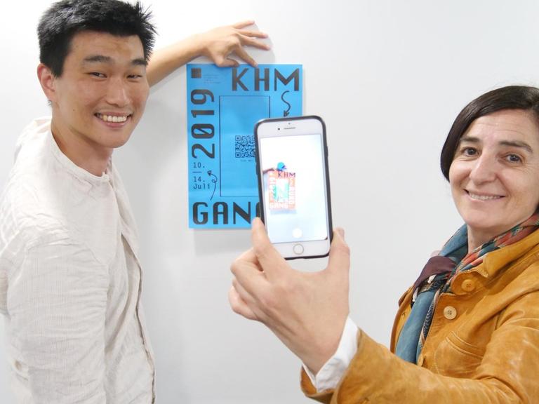 Professorin für Animation, Isabel Herguera, und Animationskünstler Sae Yun Jung präsentieren ihr Projekt "Scan Me!" und blicken durch eine spezielle App durch ihr Smartphone auf ein analoges Plakat
