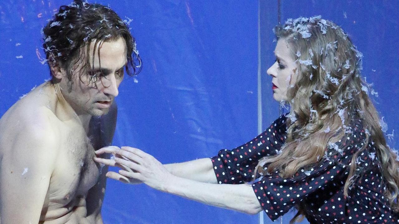 Kay, gespielt von Thomas Gräßle, mit nacktem Oberkörper. Ihm gegenüber: Gerda, gespielt von Barbara Hannigan. Sie streckt ihre Arme nach ihm aus und berührt seine Brust. Kay, gespielt von Thomas Gräßle, mit nacktem Oberkörper. Ihm gegenüber: Gerda, gespielt von Barbara Hannigan. Sie streckt ihre Arme nach ihm aus und berührt seine Brust.