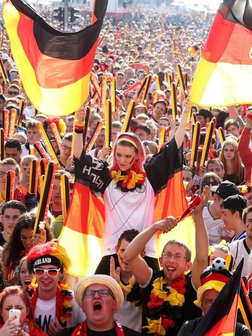 Fußballfans feiern bei der EM 2016 vor dem Brandenburger Tor. Die Szenerie ist von Deutschlandfarben bestimmt.