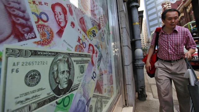 In einem Schaufenster in Hongkong sind Yuan- und Dollar-Scheine zu sehen, ein Mann geht vorbei.