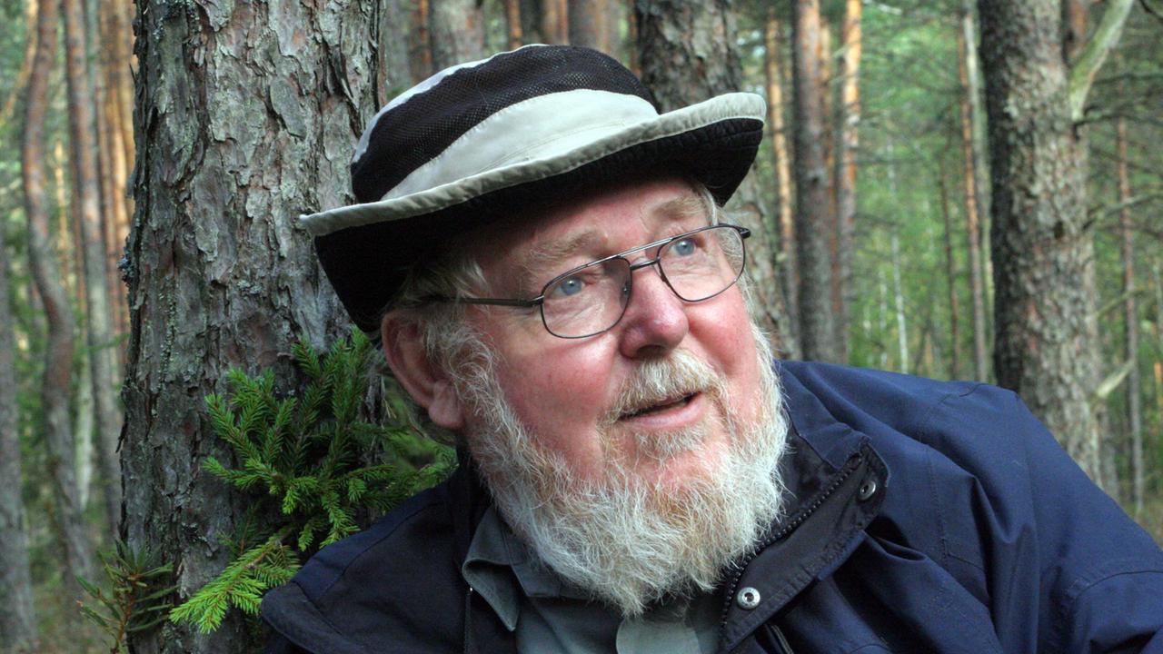 Der Biologe und Umweltschützer Michael Succow, Mütze auf dem Kopf, im Wald an einen Baum gelehnt. Der Biologe und Umweltschützer Michael Succow, Mütze auf dem Kopf, im Wald an einen Baum gelehnt.