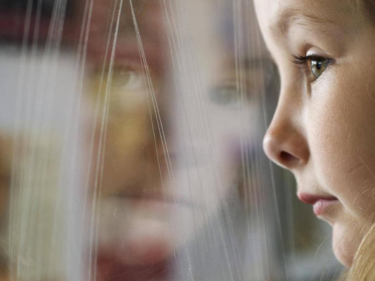 Ein junges Mädchen lehnt sich an die Glasscheibe eines Zugfensters.