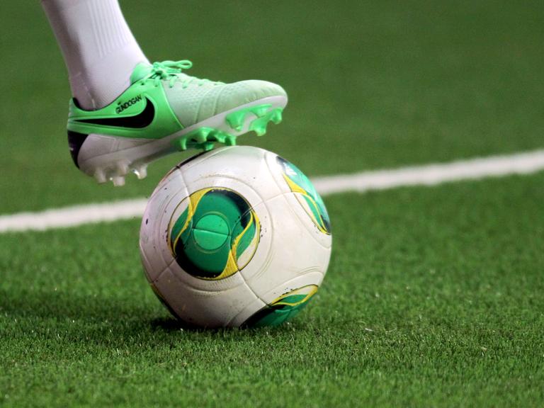Ein Fußballschuh angelegt auf einem Fußball.